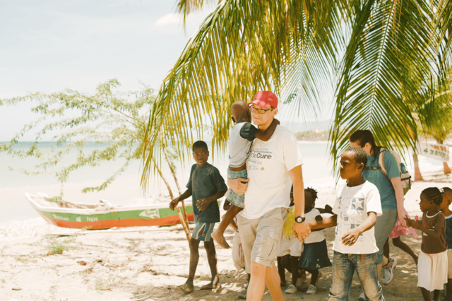 Man holding young boy , walking with other young boys in Haiti